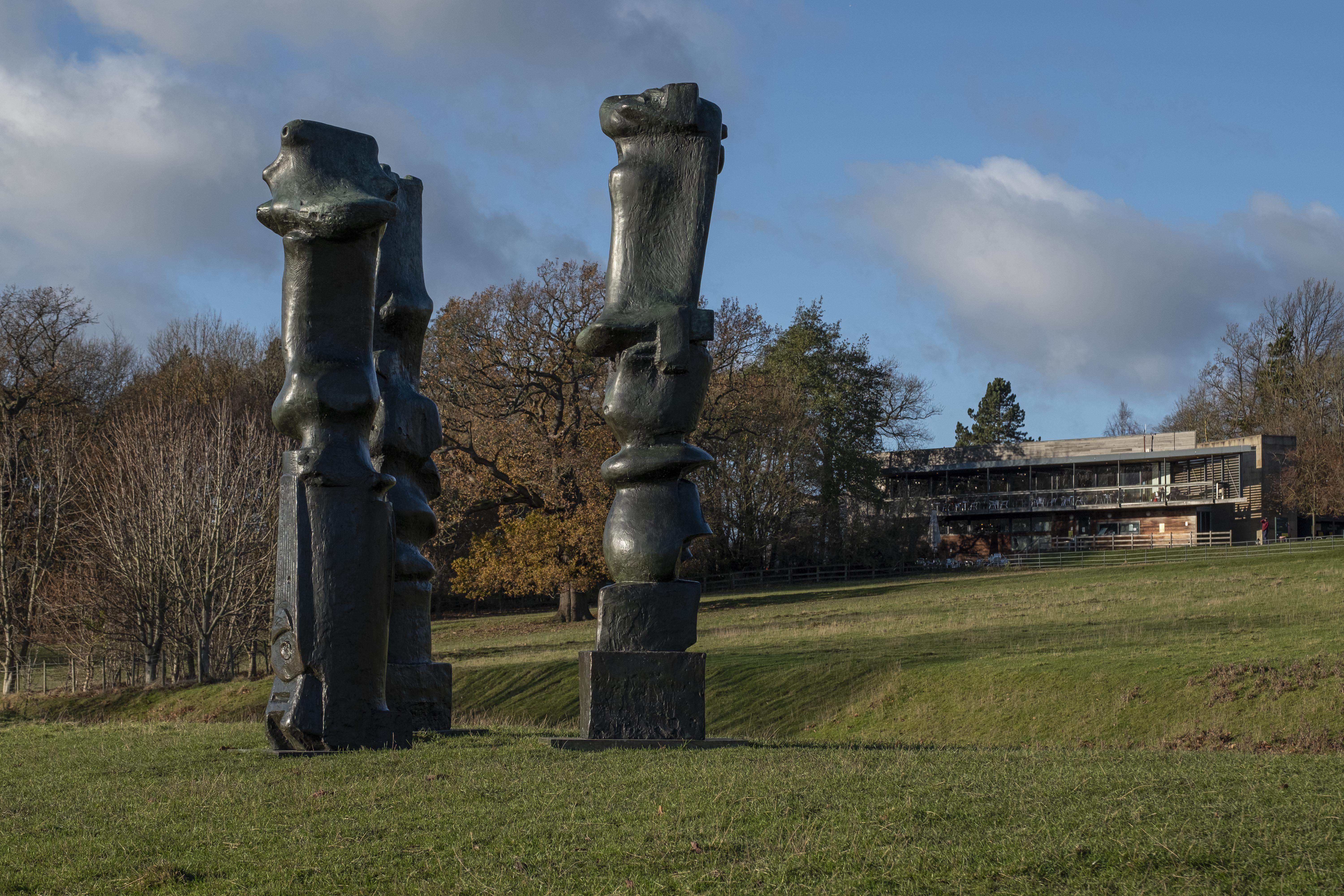 Three tall thin bronze sculptures with YSP Centre behind them