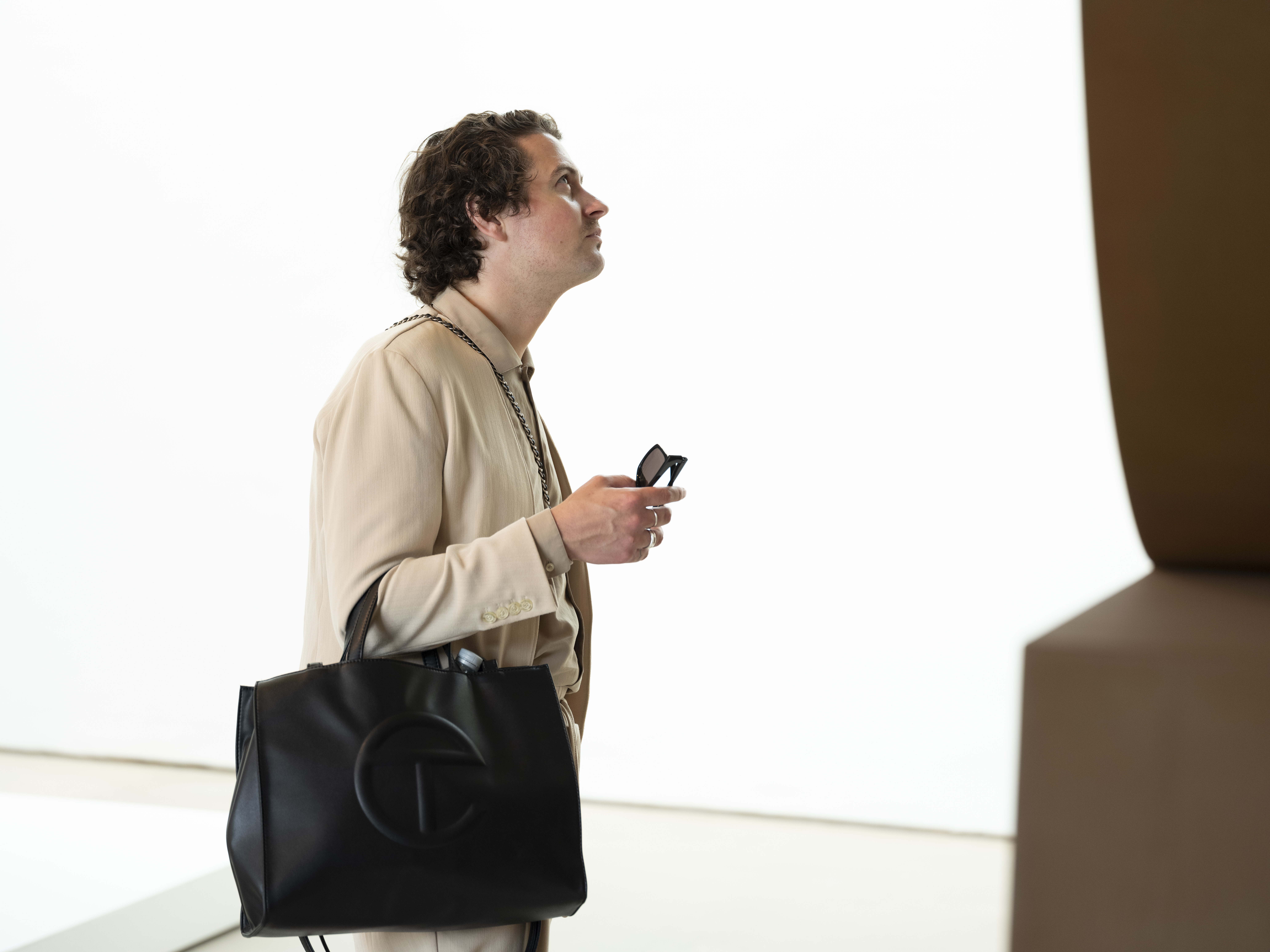 A man with a black designer bag, looking at a bronze sculpture.