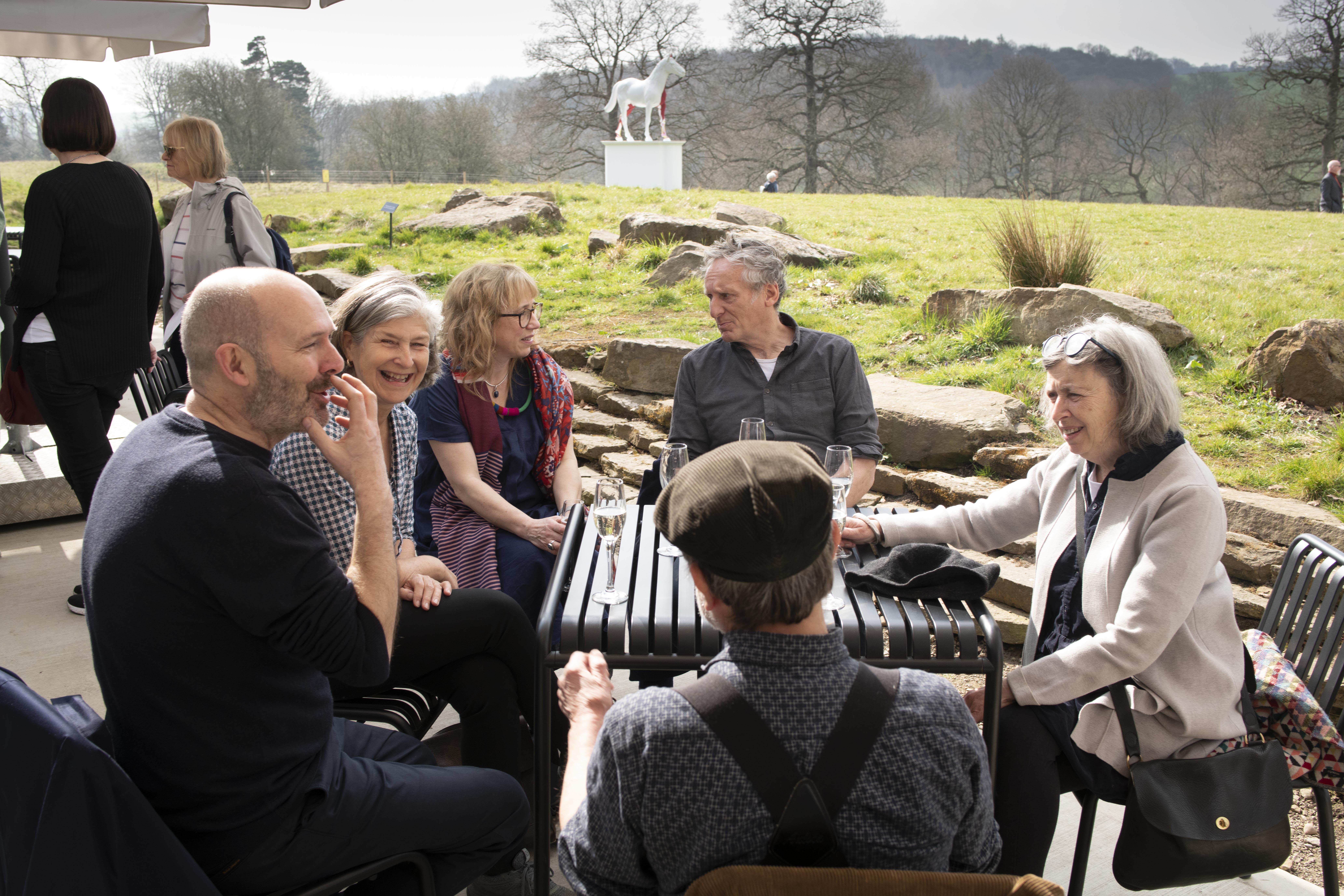 A group of people sat talking at a table outside with views overlooking YSP parkland.