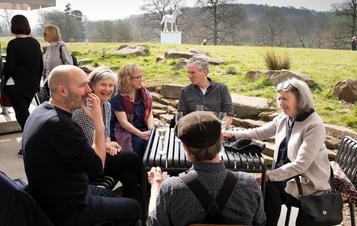 A group of people sat talking at a table outside with views overlooking YSP parkland.