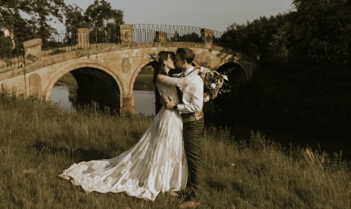 A bride and groom kissing in front of a hump-back bridge