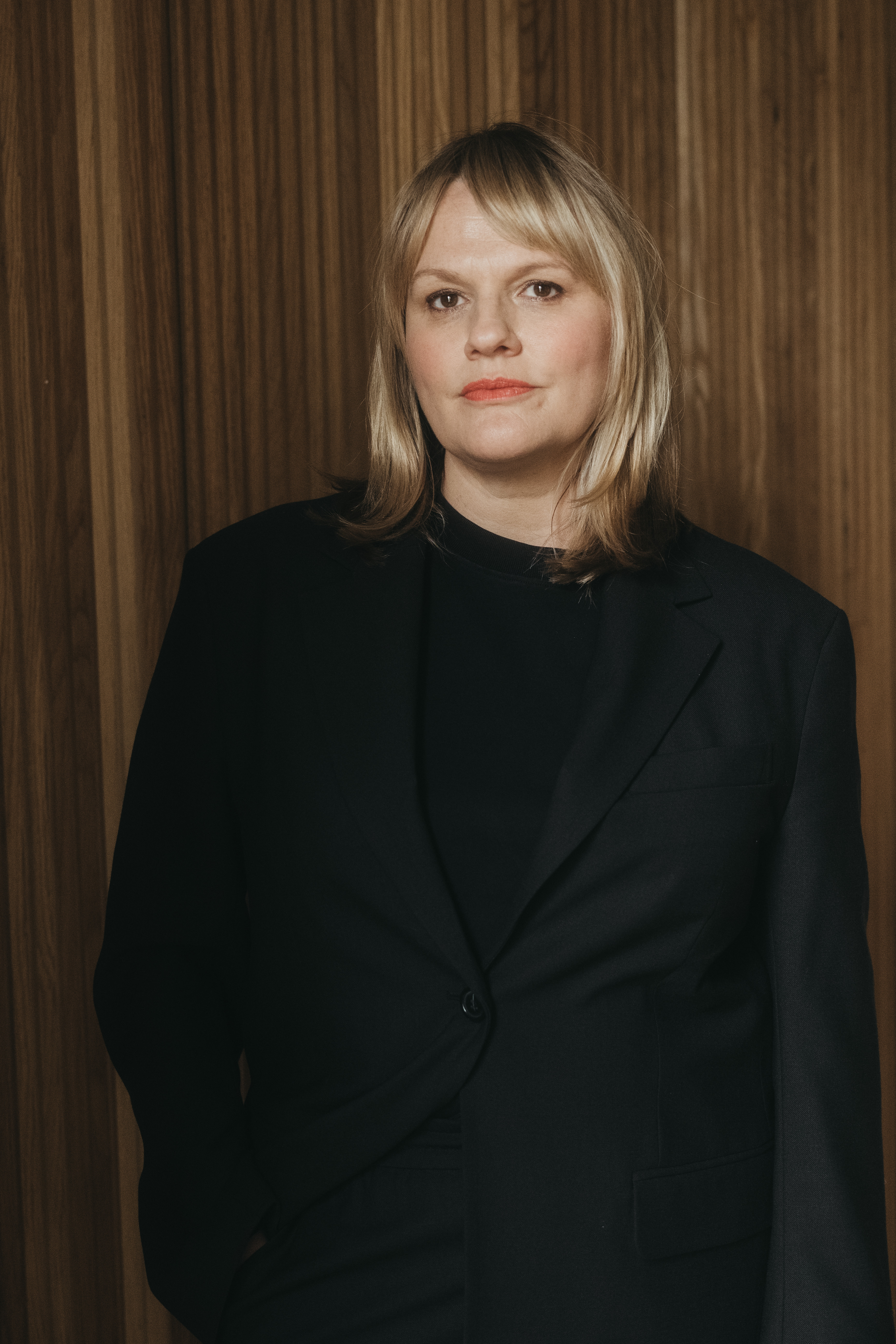 A woman with shoulder length blonde hair, wearing a black suit