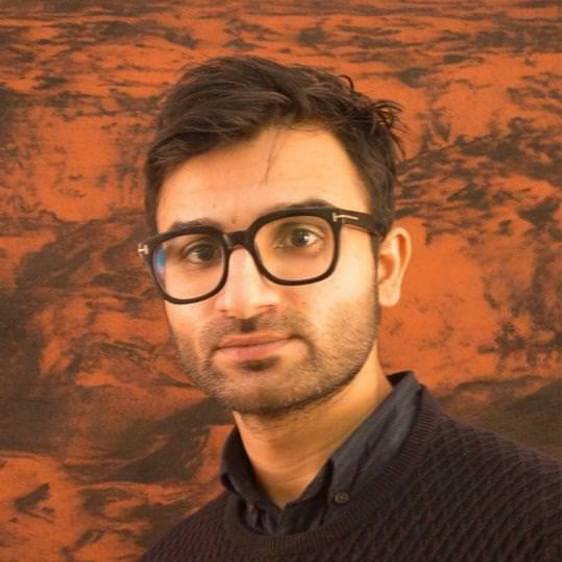 A South Asian man wearing glasses and a purple jumper