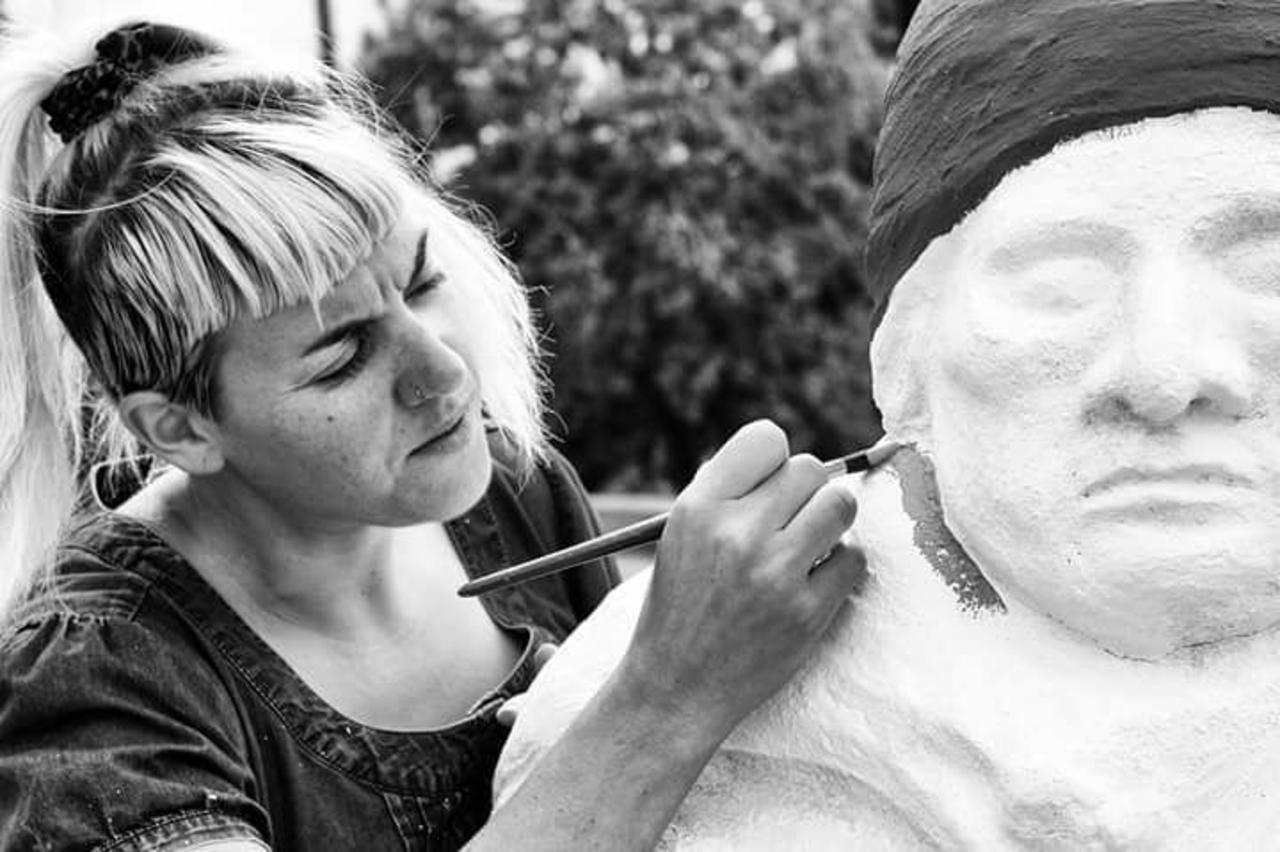 A black and white photo of a woman with a fringe painting a clay figure