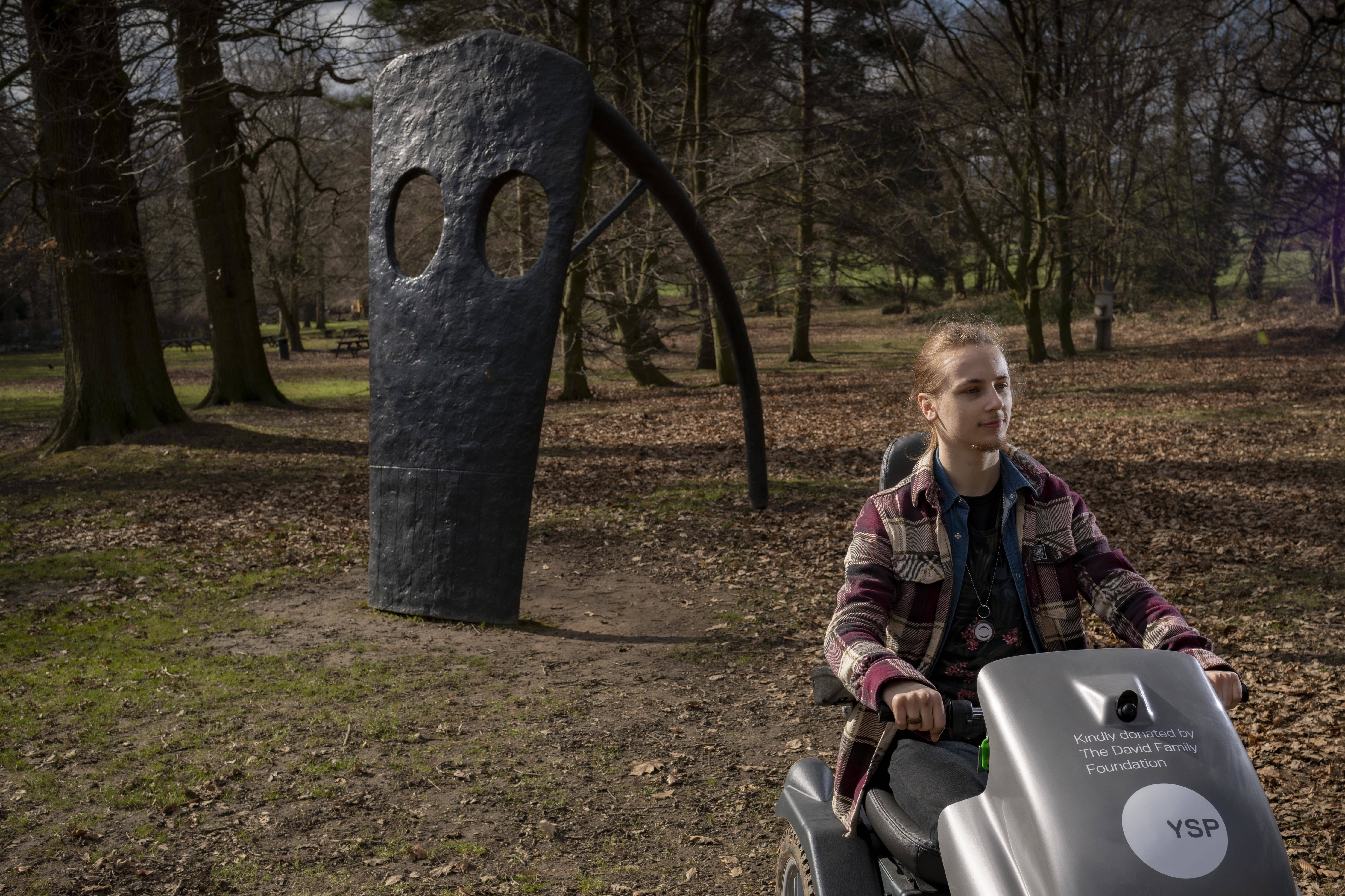 Visitor passing a sculpture in the parkland on a mobility scooter at YSP