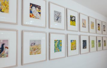 A grid of framed watercolour paintings of birds, displayed on a white gallery wall.