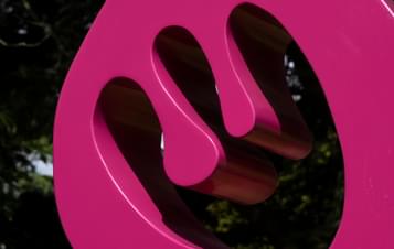 A close up of a bright pink abstract sculpture outdoors