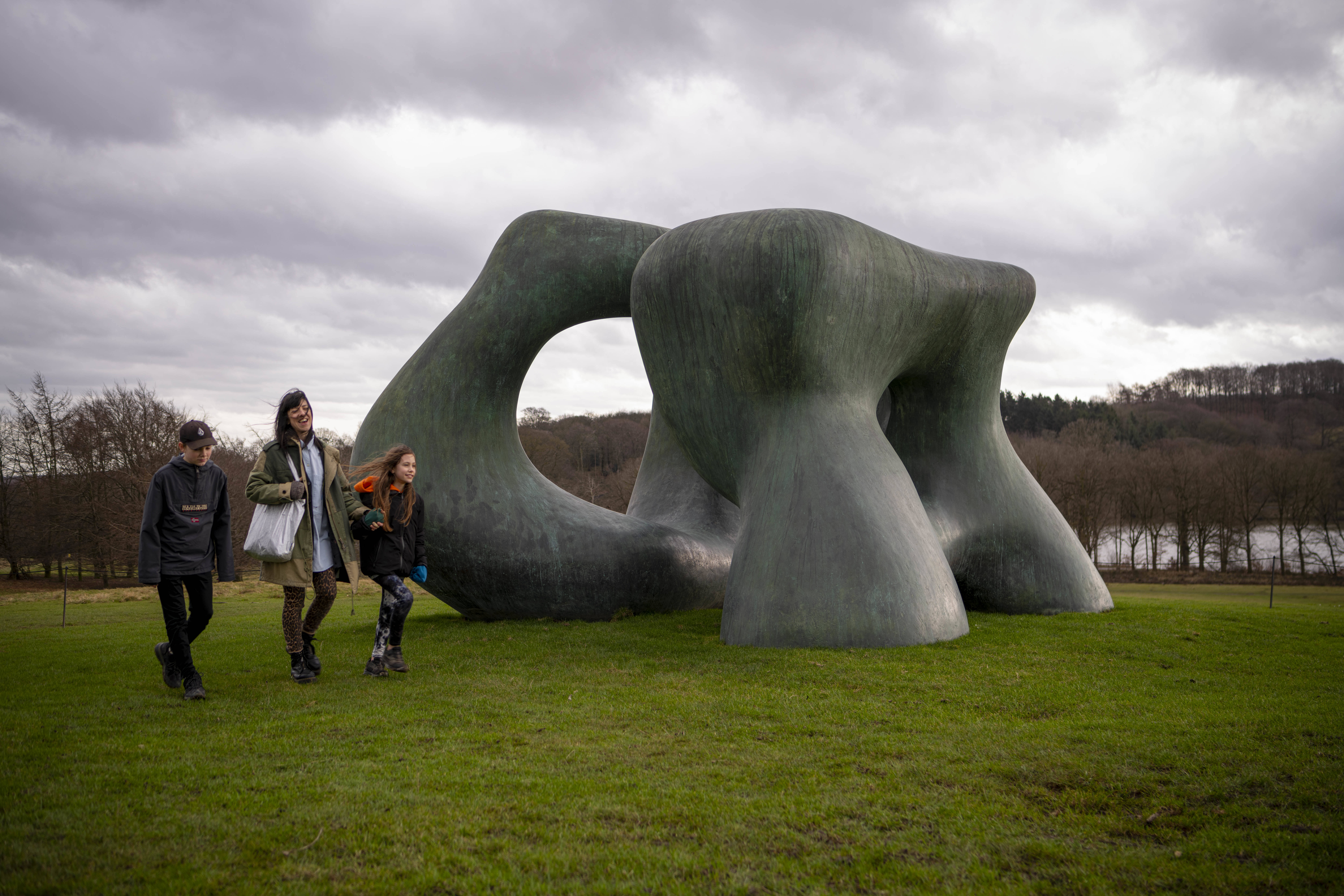 Three people walking beside Jonty Wilde Moore Large Two Forms at Yorkshire Sculpture Park
