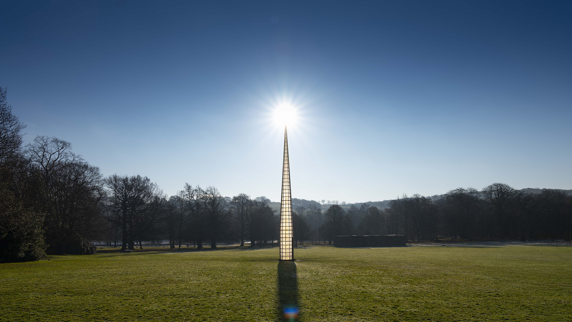A tall pointed tower, with glass panels. The sun is rising behind it.