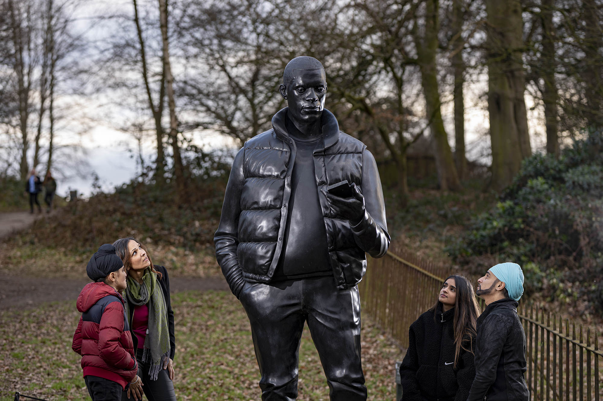 Four people looking up at a larger-than-life-size sculpture of a man holding a mobile phone.