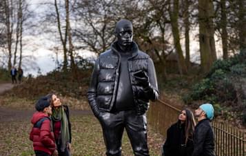 Four people looking up at a larger-than-life-size sculpture of a man holding a mobile phone.