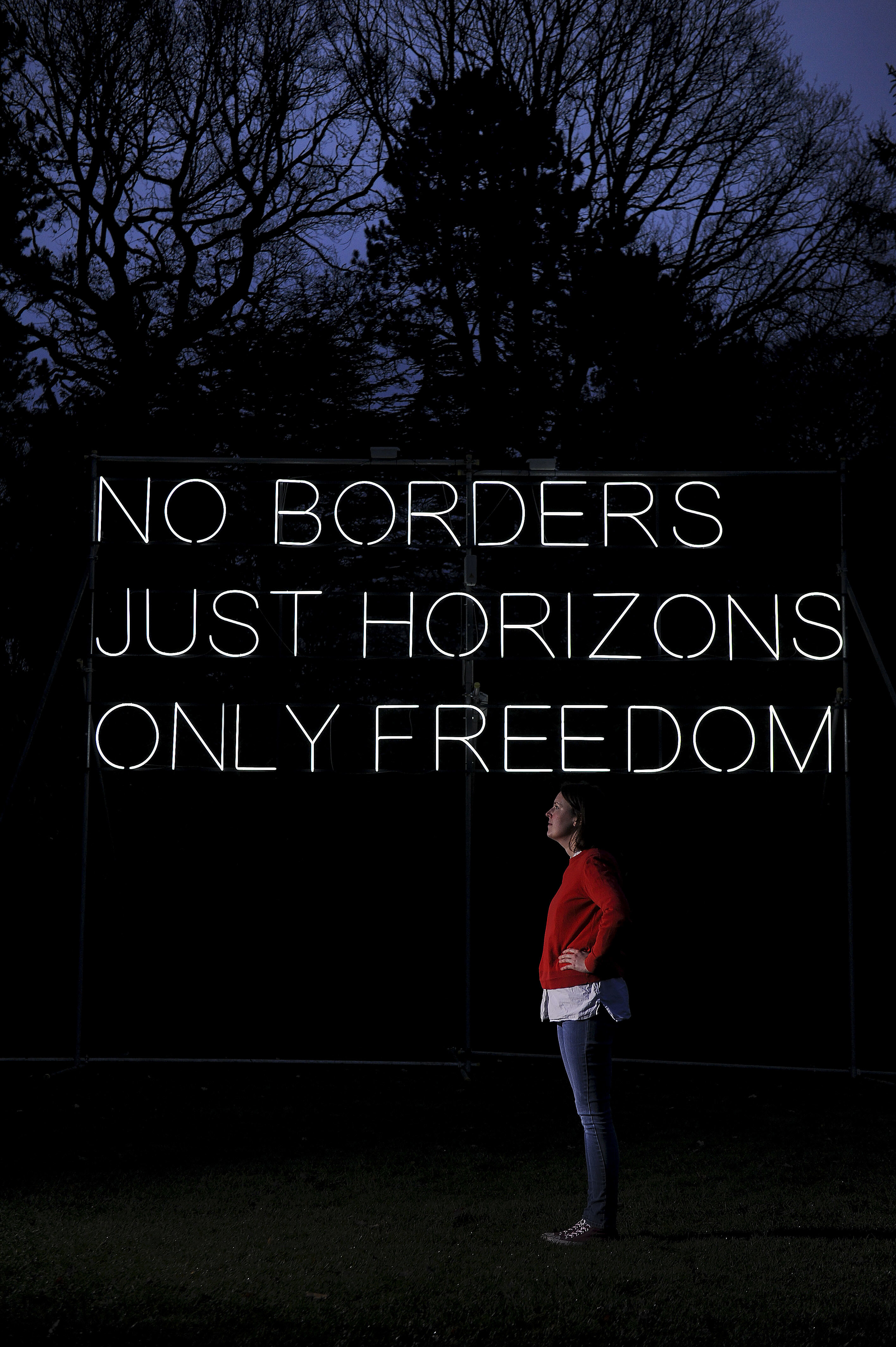A white woman standing in front of Hilary Jack No Borders 2018 lit up at Yorkshire Sculpture Park