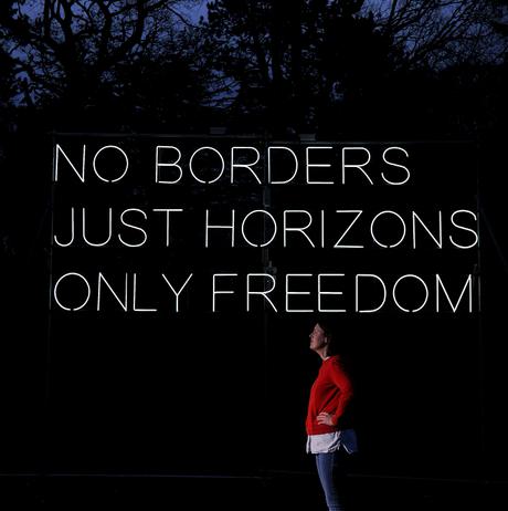 A white woman standing in front of Hilary Jack No Borders 2018 lit up at Yorkshire Sculpture Park