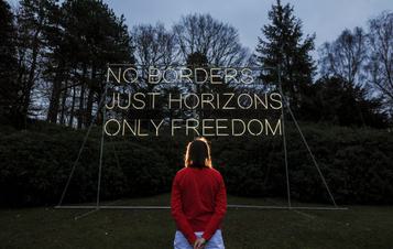 A white woman standing in front of Hilary Jack No Borders 2018 lit up at Yorkshire Sculpture Park