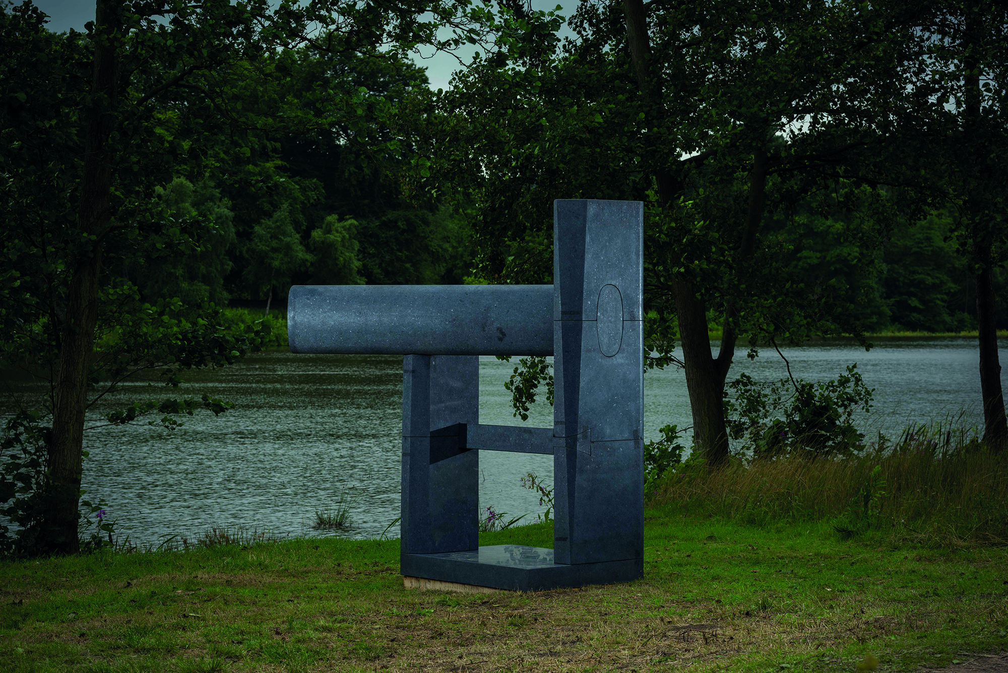 A dark grey abstract sculpture next to a lake