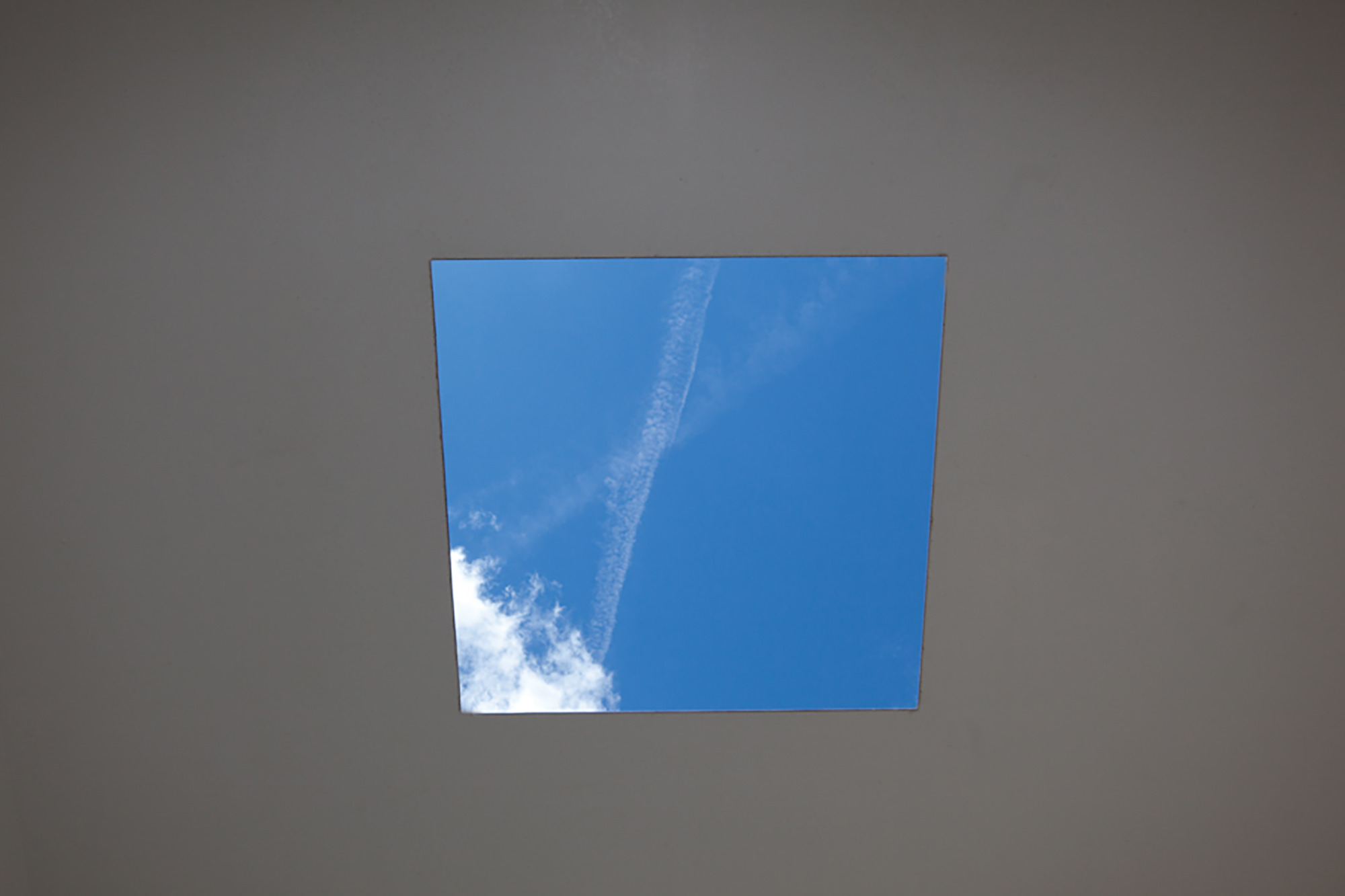 The view through a square hole in the roof of Skyspace, showing a blue sky with clouds and airplane trails