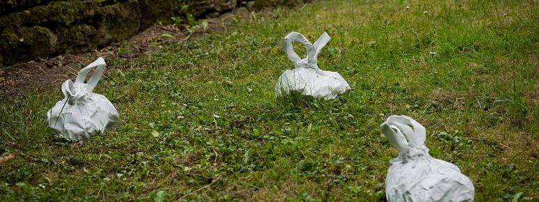 A group of white sculptures in the shape of dog-poo bags, on grass