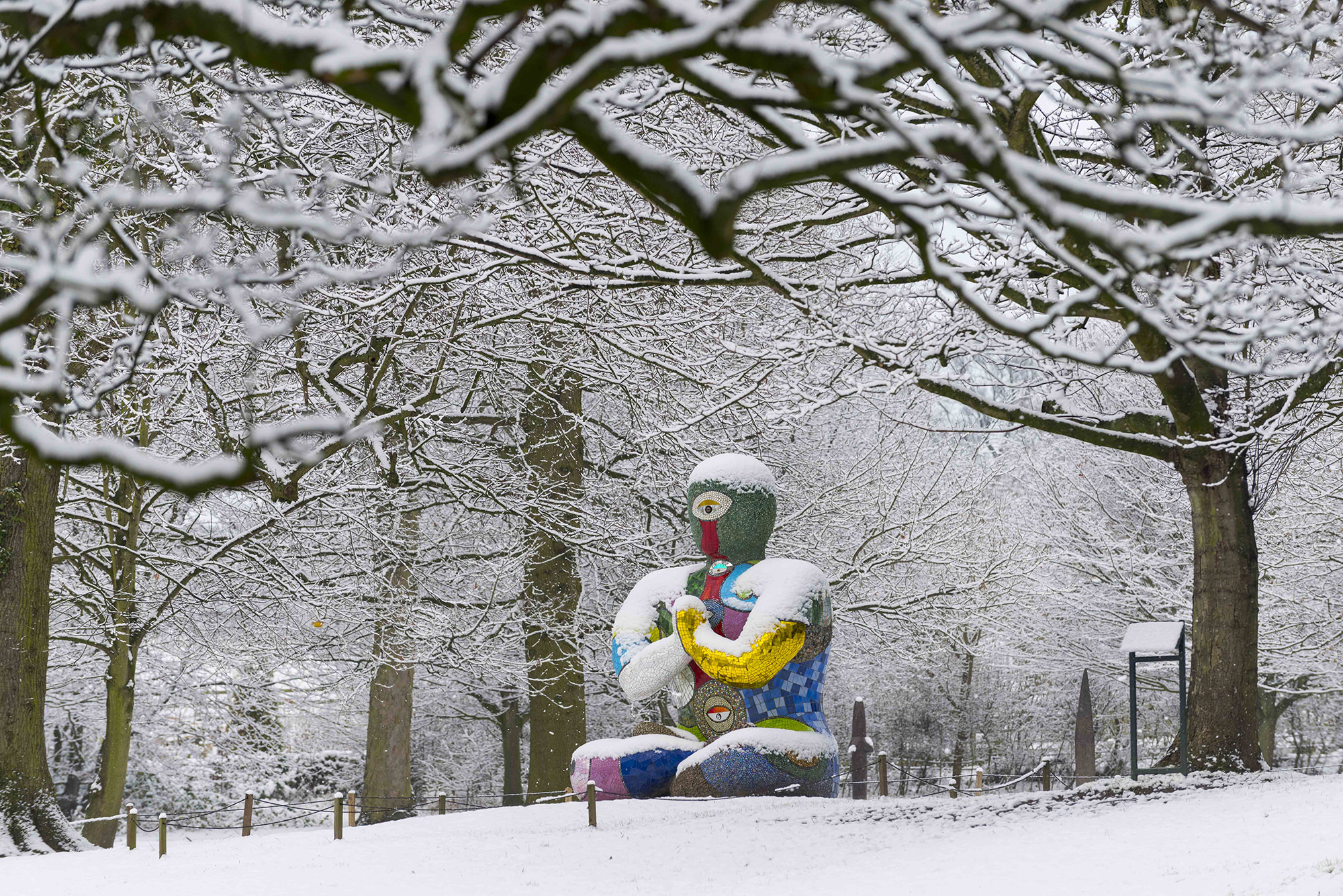 A seated humanoid figure covered in brightly coloured mosaic tiles in the snow