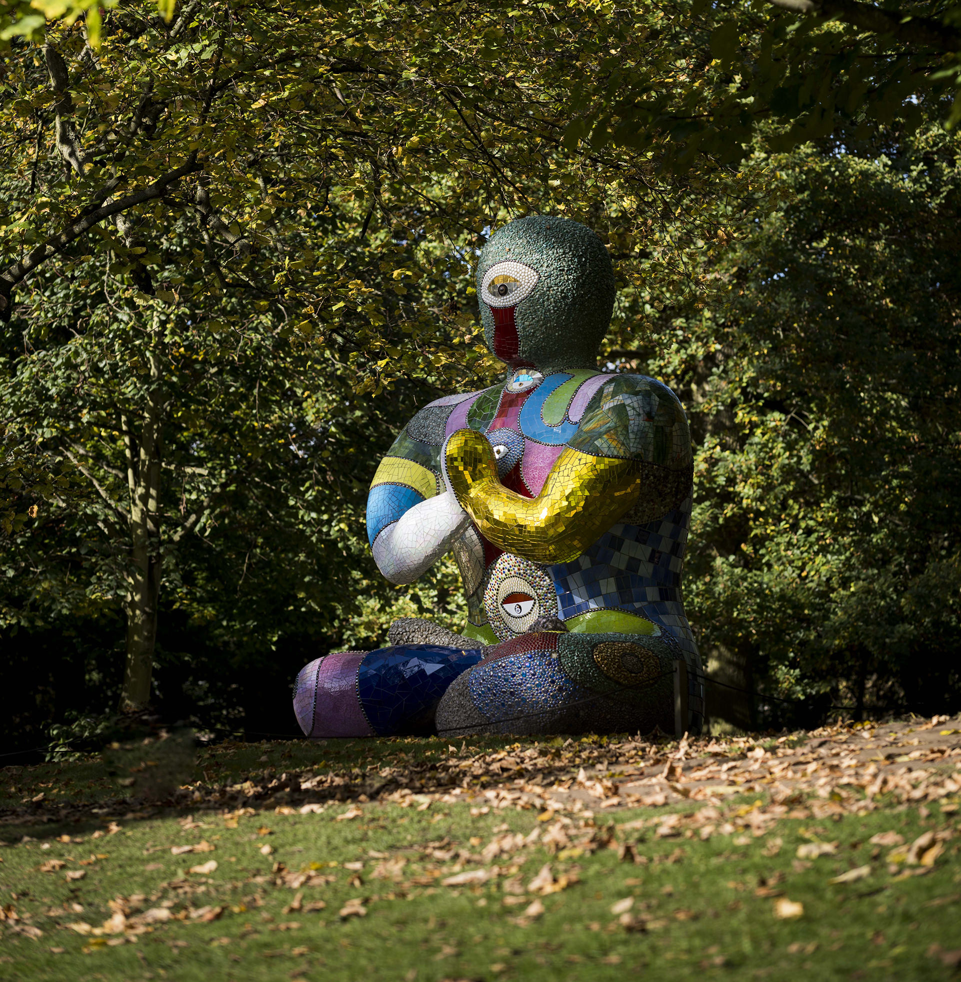 A seated humanoid figure covered in brightly coloured mosaic tiles