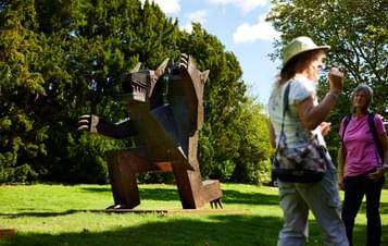 A group of people standing near to a 2 headed bear sculpture outdoors