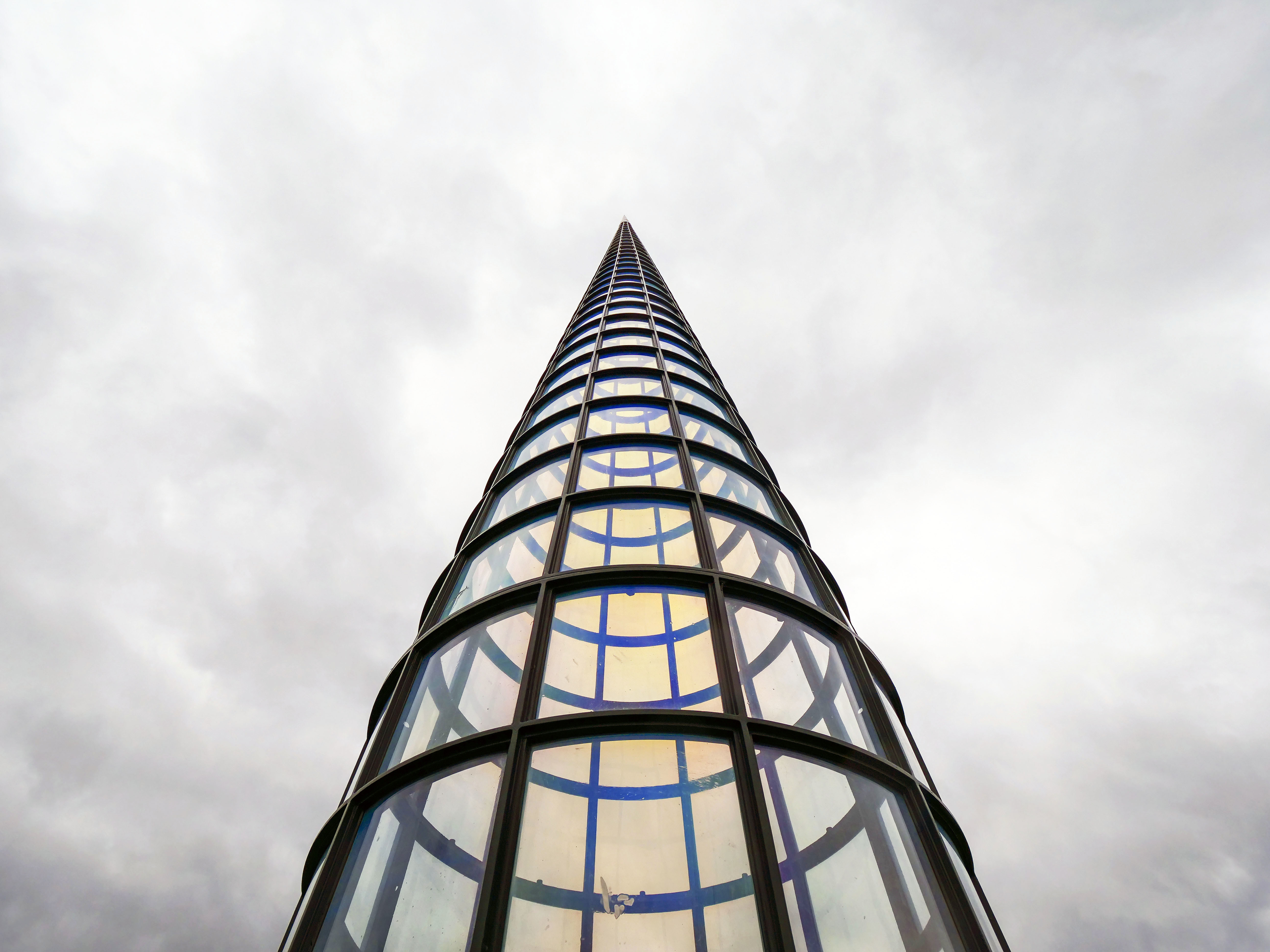 Looking up towards a tall pointed tower, with glass panels