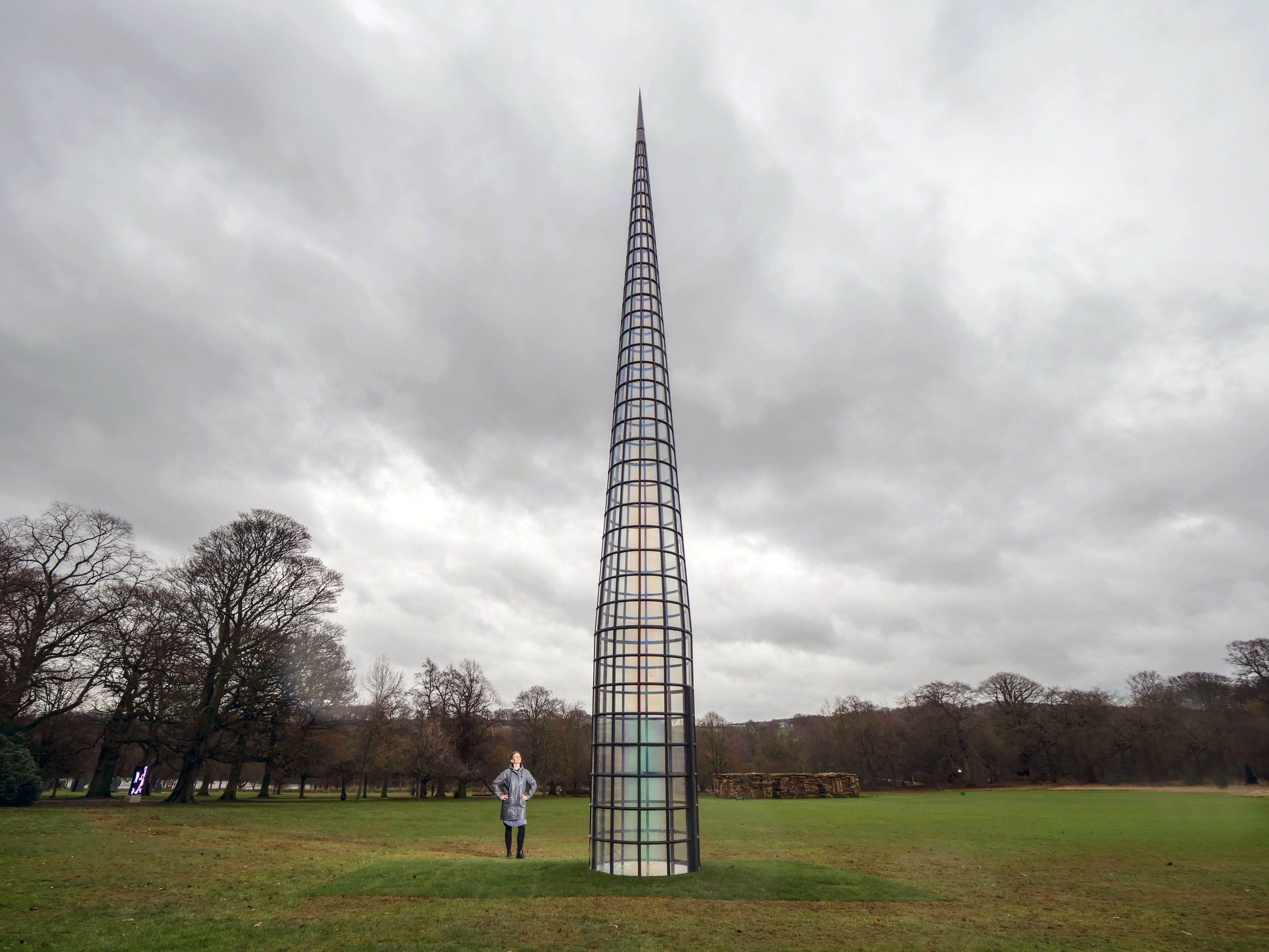 A person walking towards a tall pointed tower, with glass panels