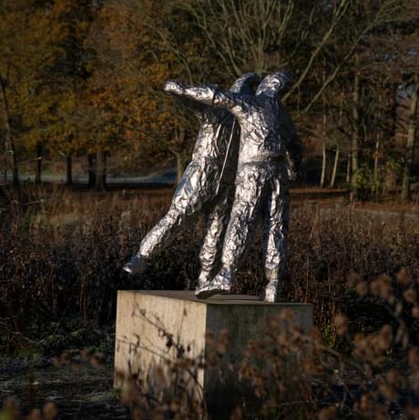 Two silver figures in astronaut suits with flat expressionless faces, in an embrace