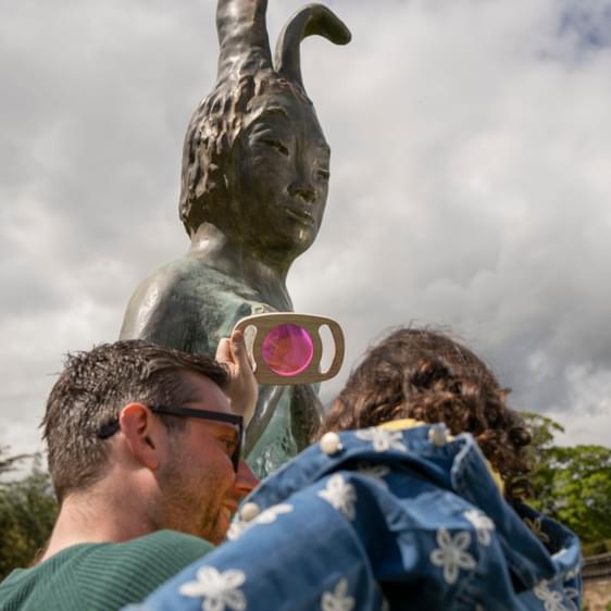 An adult and child looking at a rabbit shaped sculpture through a coloured viewfinder.
