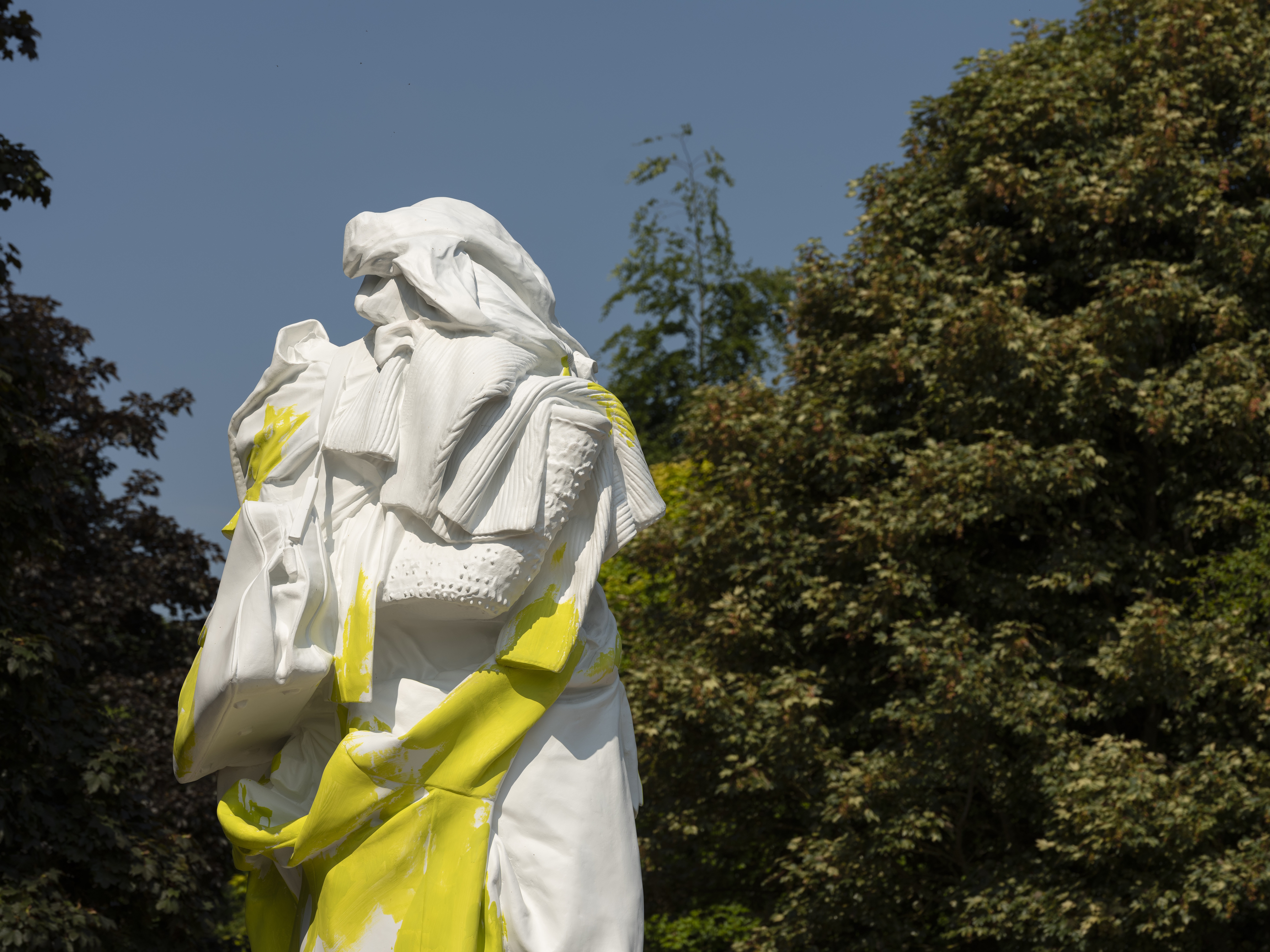 A yellow and white sculpture of a figure draped in clothing