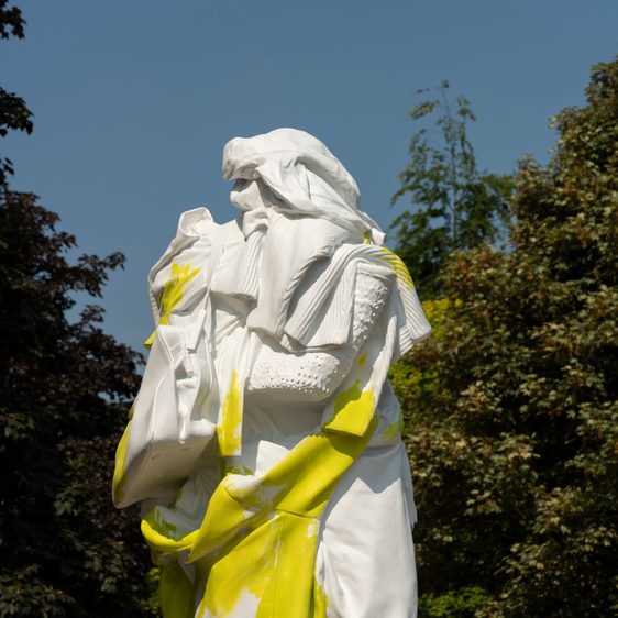 A yellow and white sculpture of a figure draped in clothing