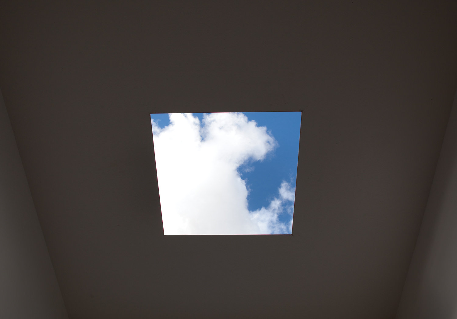 The view through a square hole in the roof of Skyspace, showing a blue sky with clouds.