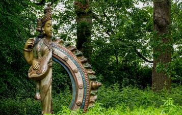 A sculpture of a deity with stands amidst lush greenery, surrounded by tall trees.