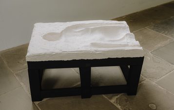 A plaster mould of a human head and torso with ridged sections displayed on a black plinth on a stone floor.