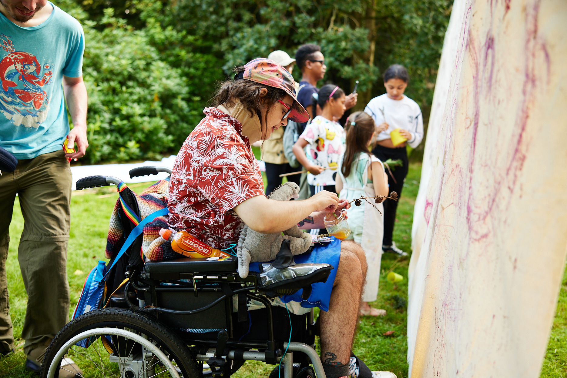 A wheelchair user painting onto a piece of suspended fabric outdoors.