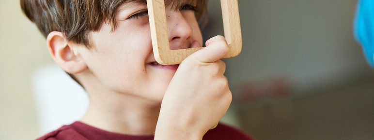 A child holding a square wooden viewfinder to his face.
