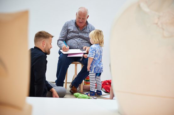 Two men with a child, one sat down on a chair drawing and another on the floor