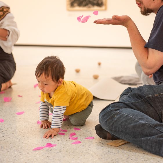 A baby crawling through confetti being blown by their adult.