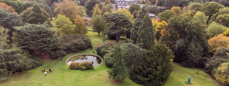 An aerial photograph of a formal garden with large trees, bronze classical sculptures and people.