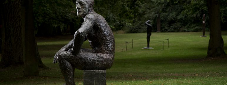 A bronze seated figure, displayed outdoors.