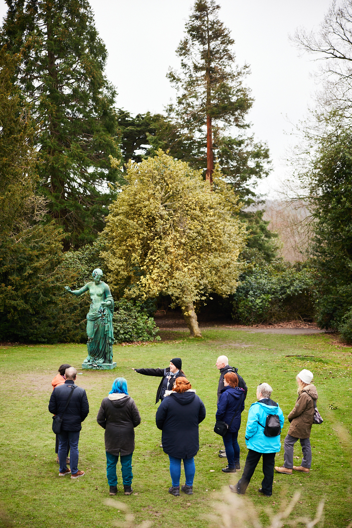 A group of people and a guide looking at a bronze sculpture of a woman outdoors