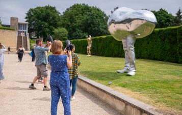 A group of people taking photographs of an oval silver sculpture with legs.