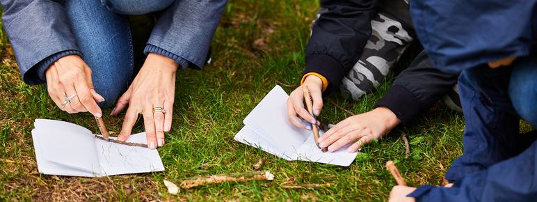 Three people kneeling on the grass, drawing in sketchbooks.