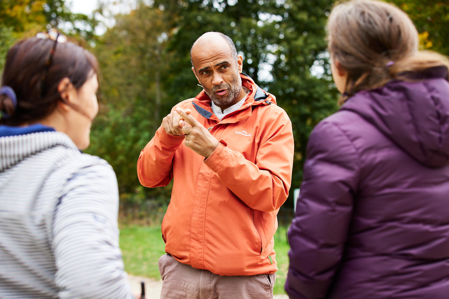 A man in an orange coat doing sign language outdoors