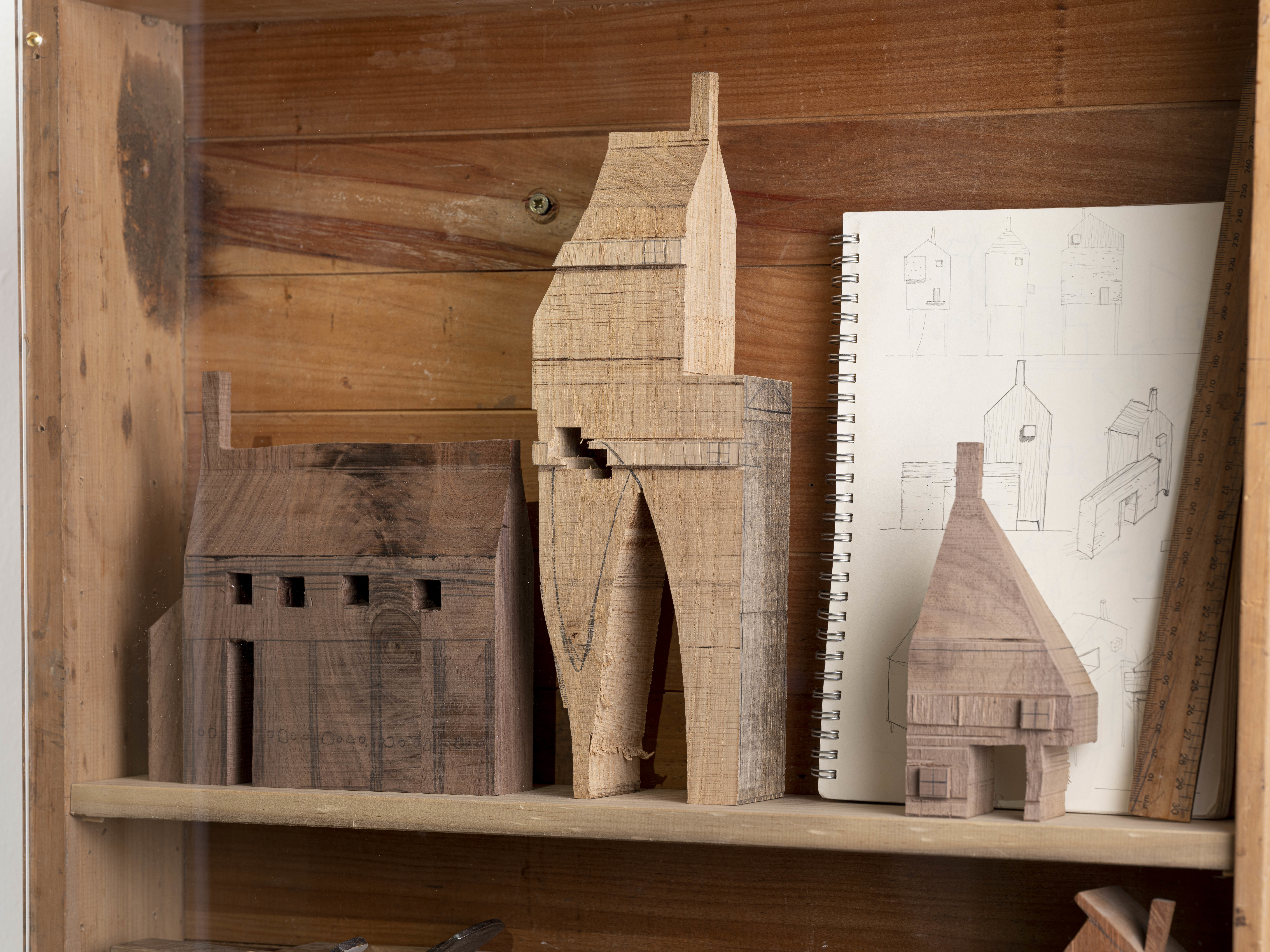 Three miniature wooden houses and a pencil drawing of a house on a shelf.