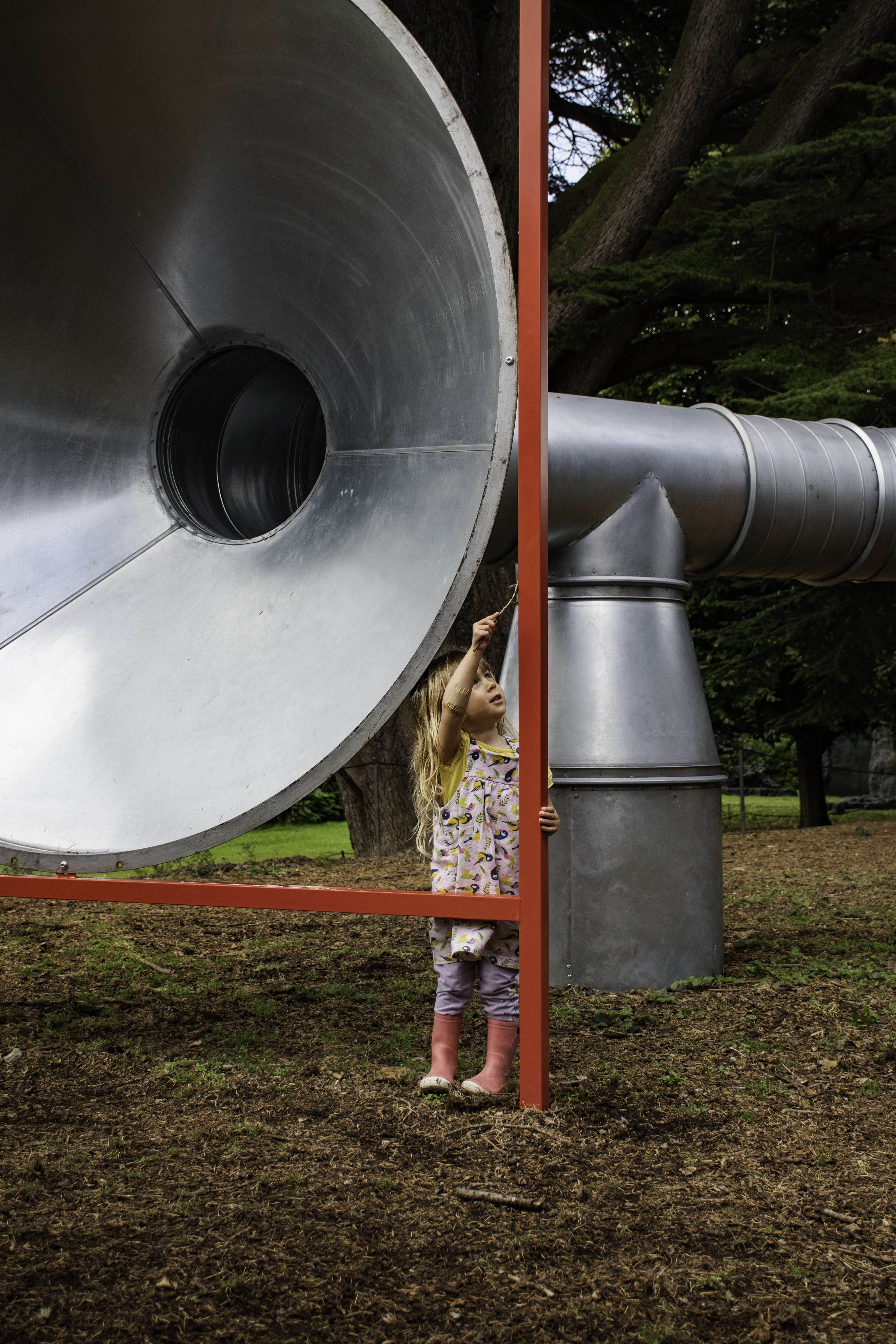 A child touching a giant silver tube with a stick
