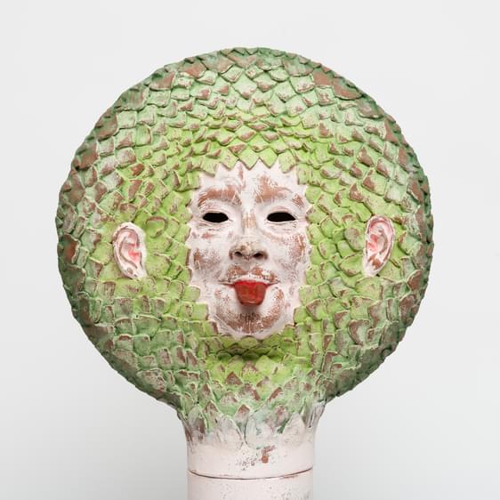 A ceramic face with it's tongue out, with green leaf-like hair.