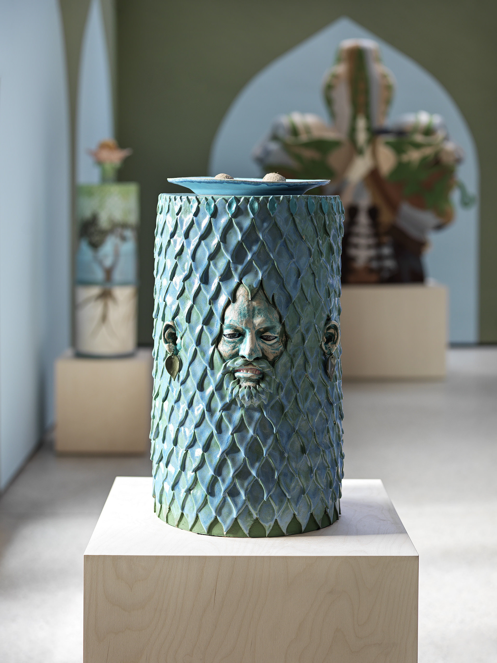 A turquoise cylindrical ceramic work with a face emerging from it.