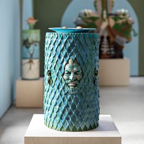 A turquoise cylindrical ceramic work with a face emerging from it.