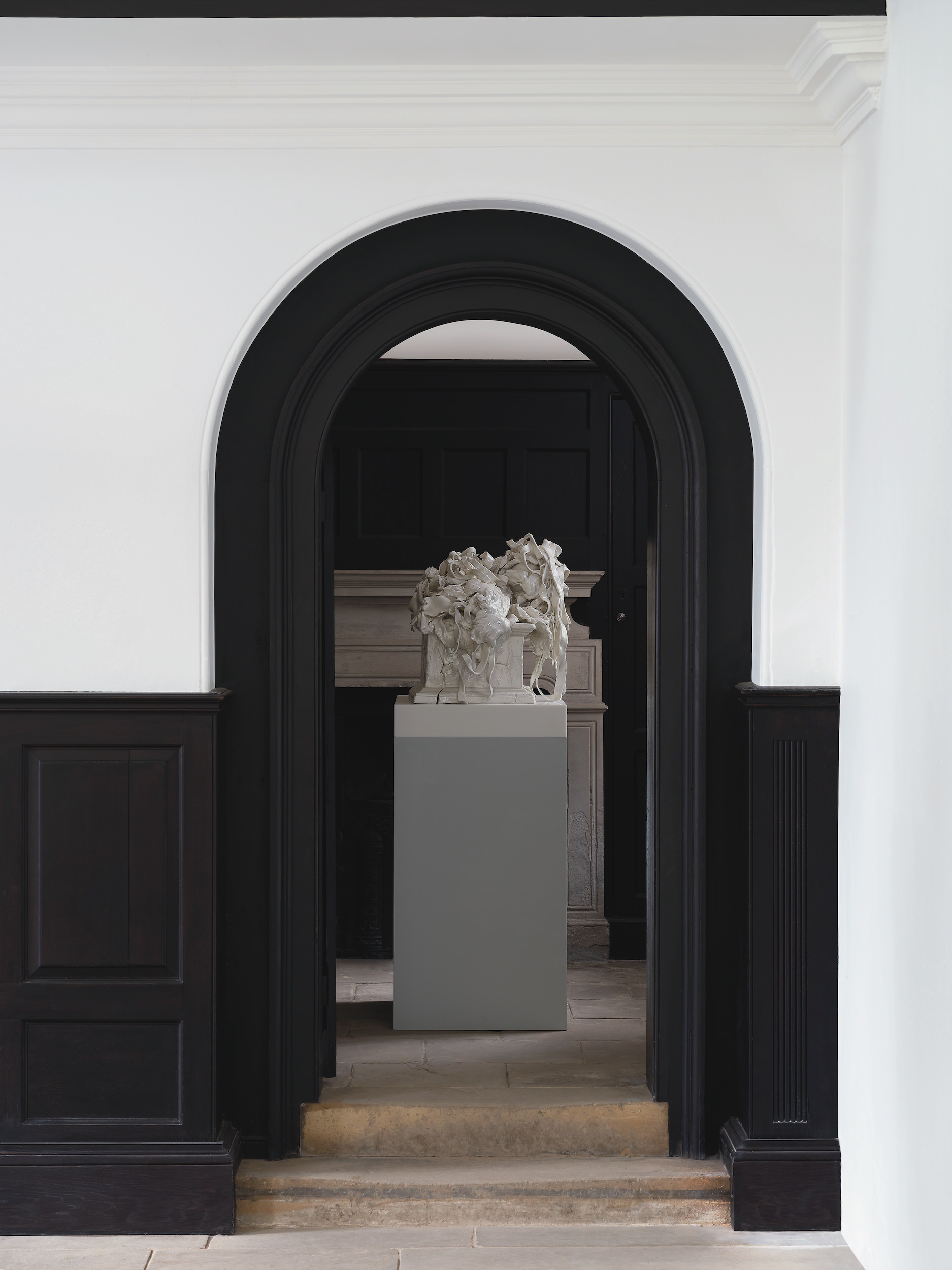 Porcelain sculpture on a plinth, framed by a black arched door way.