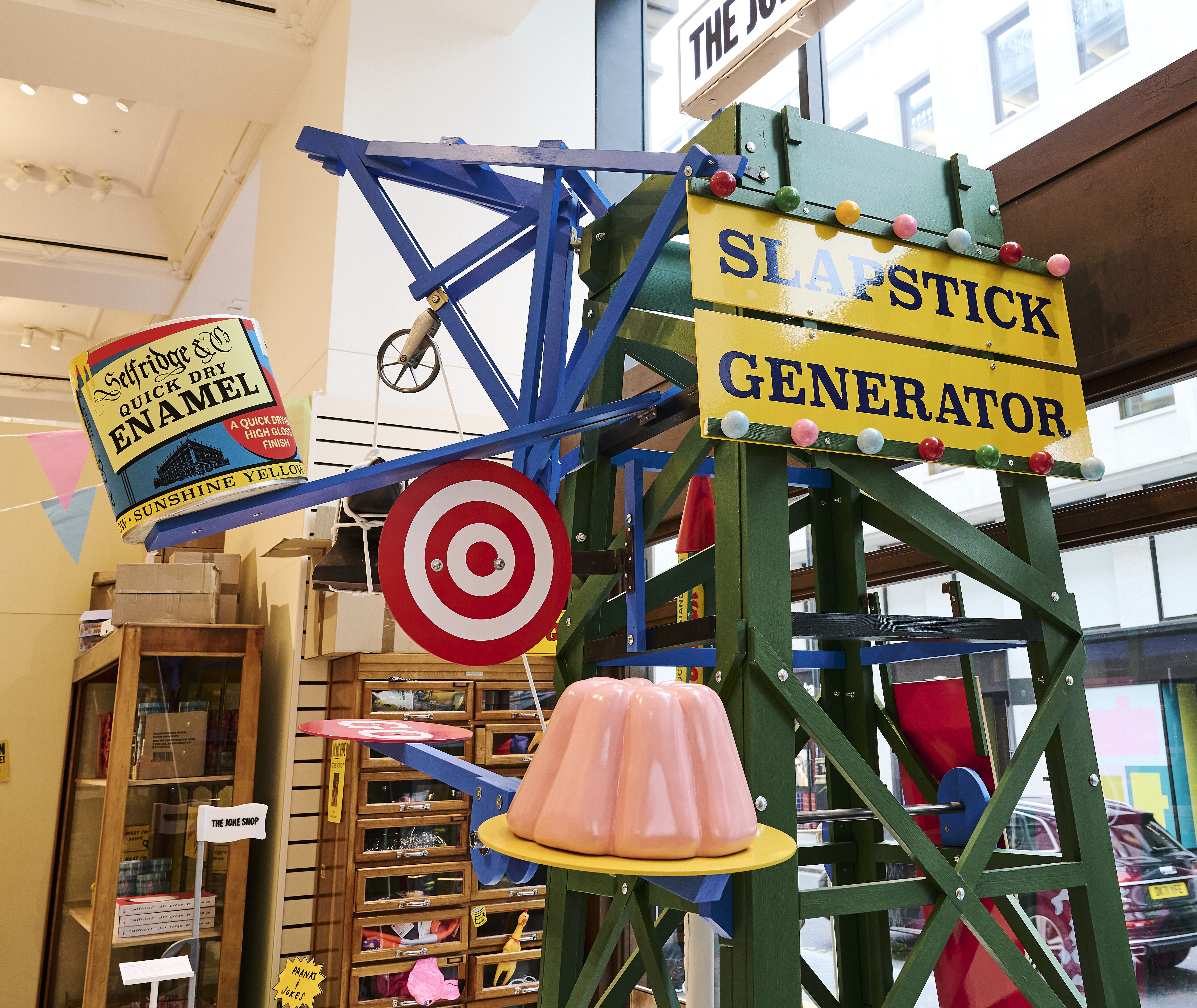 A colourful scaffolding structure with giant targets, models of jelly and paint cans. A sign reads SLAPSTICK GENERATOR